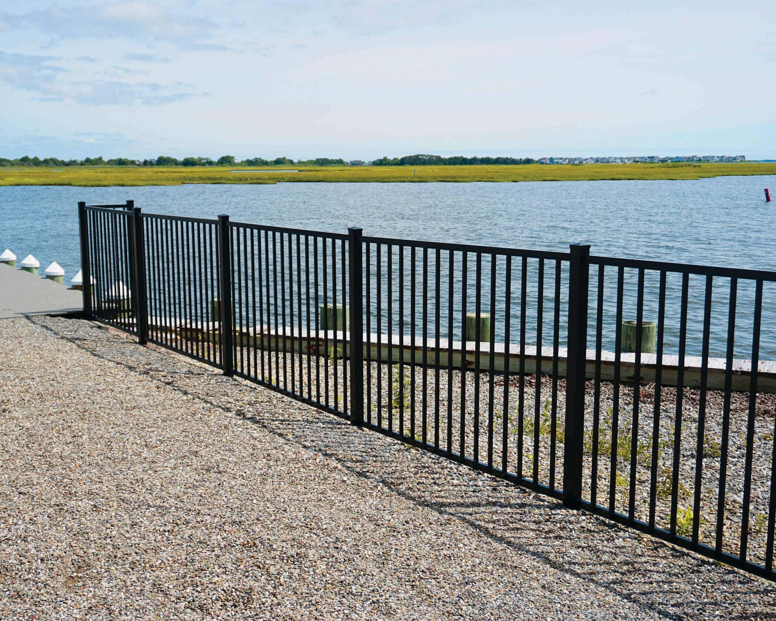 The edge of a property on the bay, with the dock and seawater in the background. The property is lined with Active Yards Bedrock aluminum fencing.